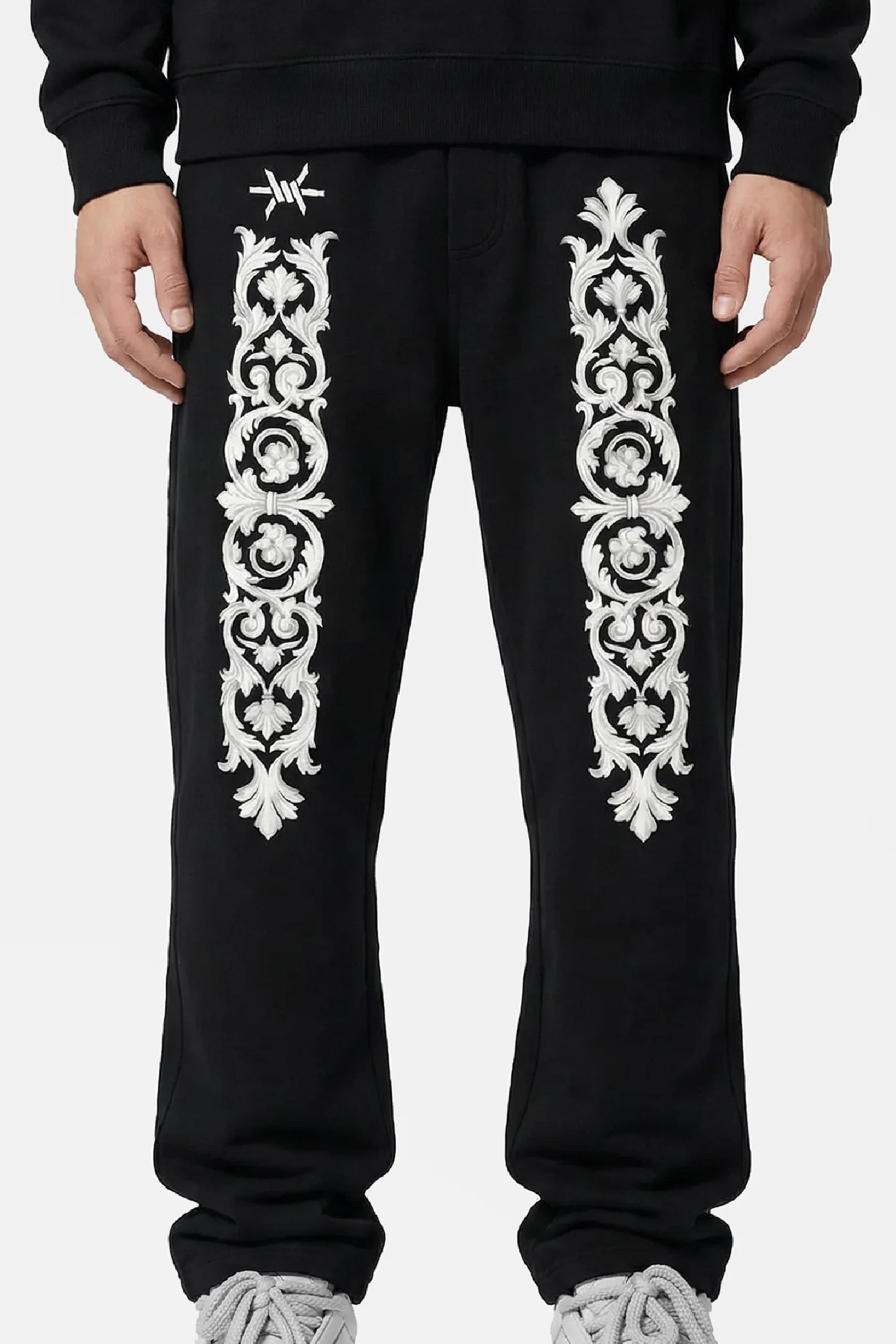Man wearing black sweatpants with white floral baroque patterns and 'Ominous' brand logo on a white background