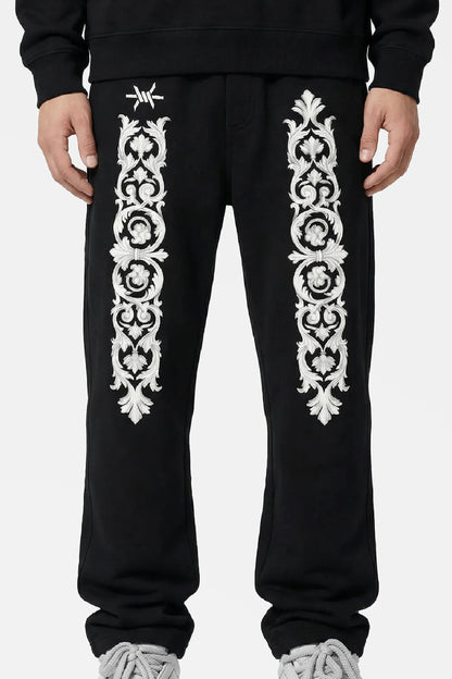 Man wearing black sweatpants with white floral baroque patterns and 'Ominous' brand logo on a white background