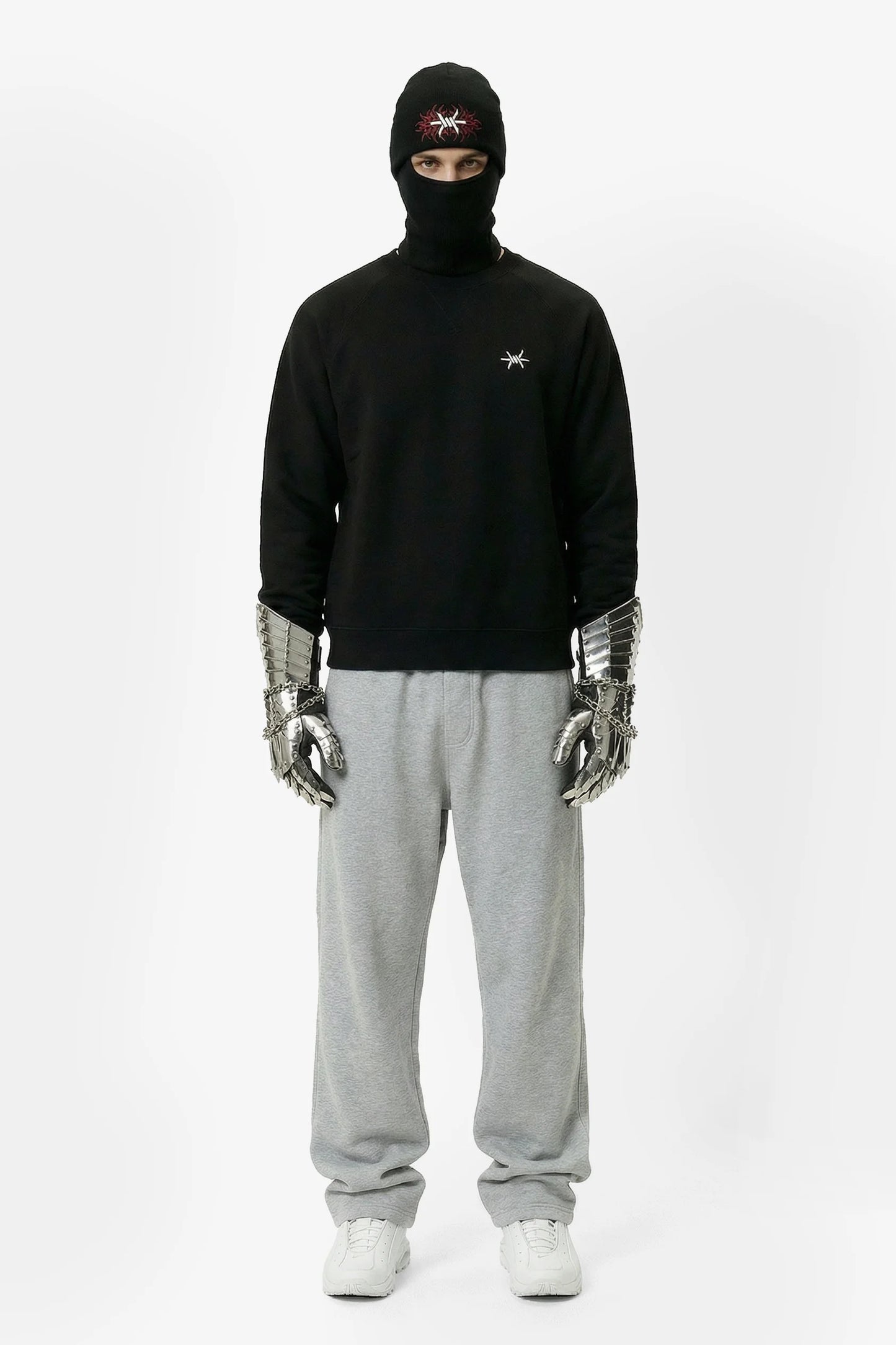 Person wearing a black hoodie, gray sweatpants, and silver gloves on a white background