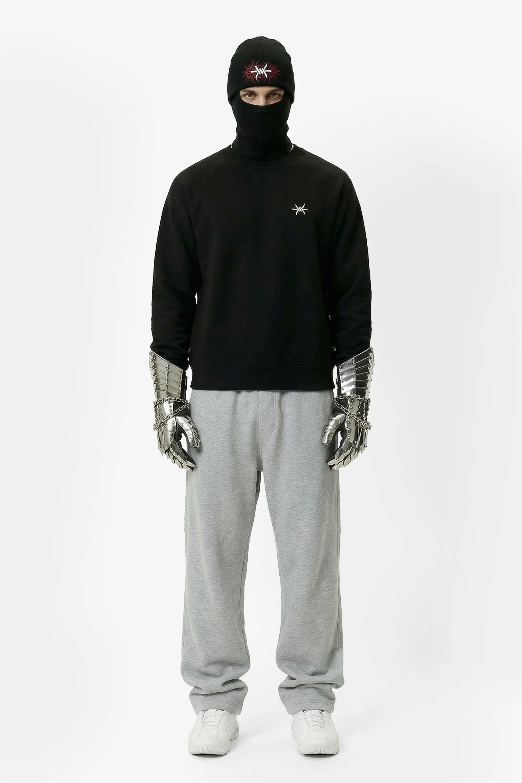 Person wearing a black hoodie, gray sweatpants, and silver gloves on a white background