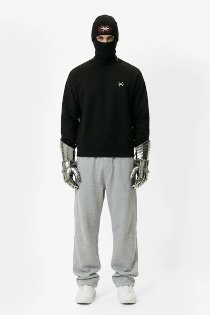 Person wearing a black hoodie, gray sweatpants, and silver gloves on a white background