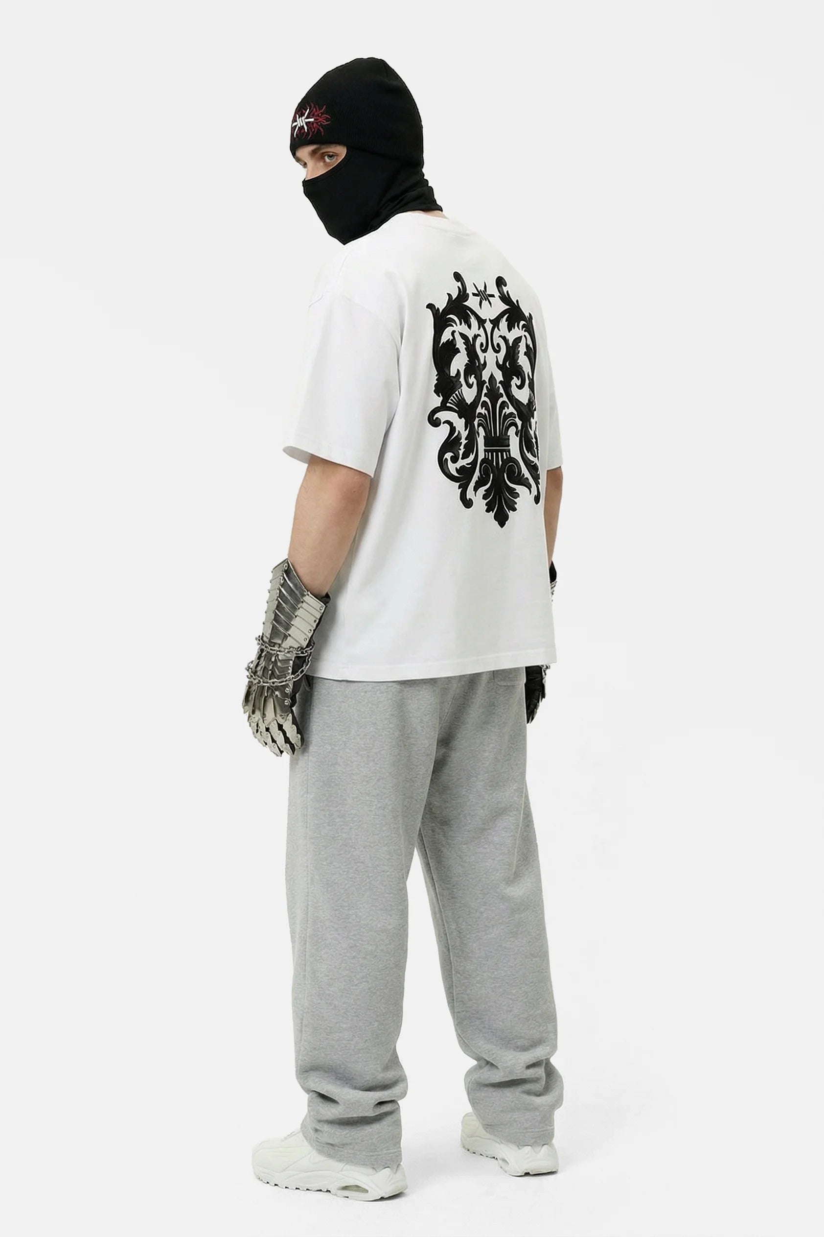 Person wearing a white t-shirt with a black design, gray pants, and a black balaclava on a white background
