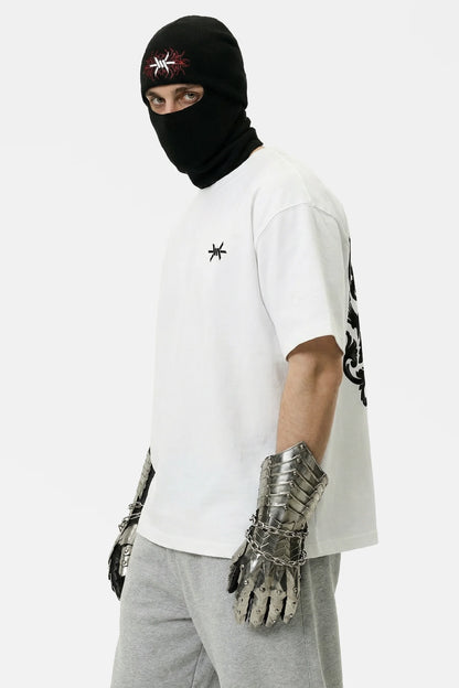 Person wearing a white t-shirt with black designs, gray pants, and metallic gloves on a white background.
