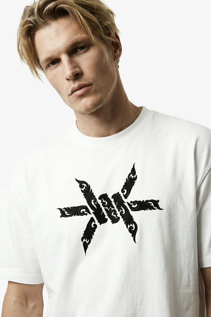 Man wearing a white t-shirt with a black baroque 'Ominous' brand logo on a white background