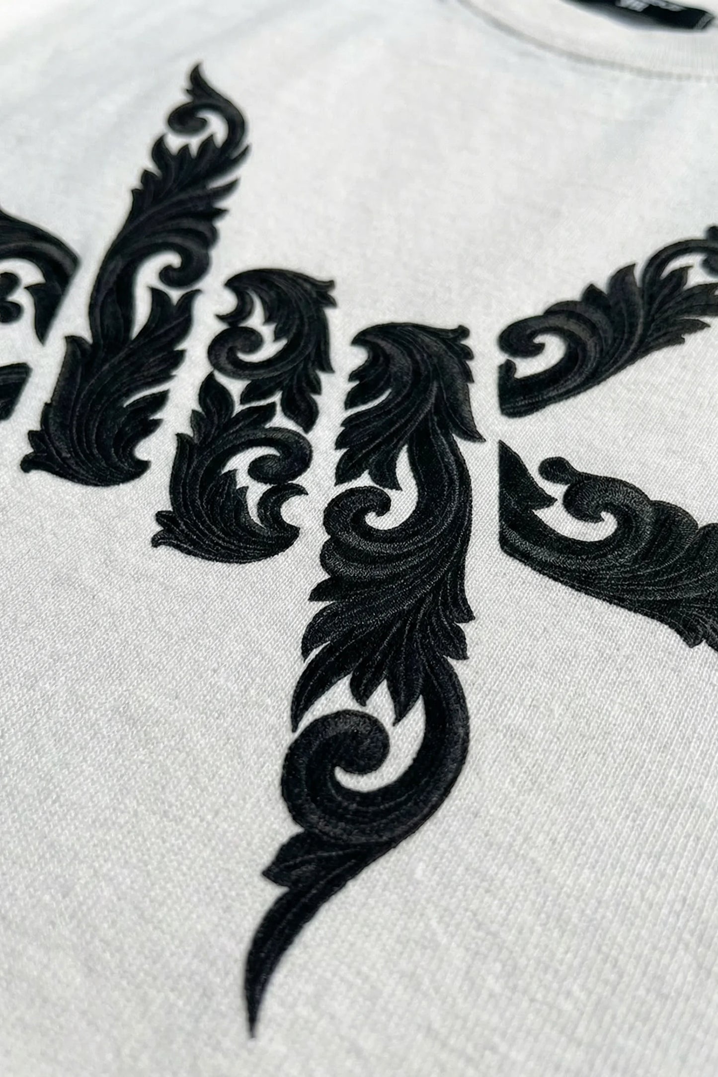 Close up of black floral embroidery style logo print on a white luxury 'Ominous' brand t-shirt
